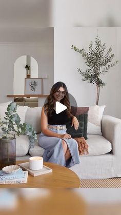 a woman sitting on top of a couch in a living room next to a plant