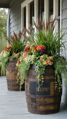 three wooden barrel planters filled with flowers and plants sitting on a porch next to a house