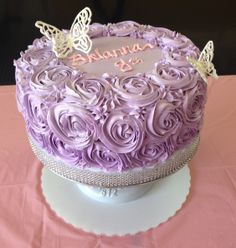 a birthday cake with purple frosting and butterflies on top, sitting on a pink tablecloth