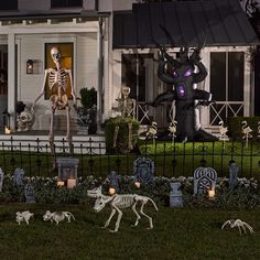 halloween decorations in front of a house with skeletons and cats on the lawn at night