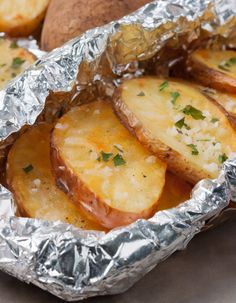 baked potatoes in foil with parsley on top and garlic on the side, ready to be eaten