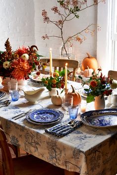 the table is set with blue and white plates, flowers, candles and pumpkins