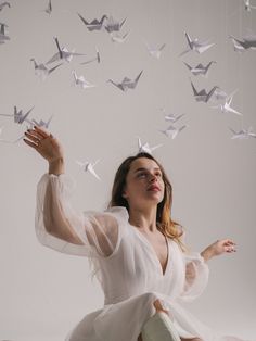 a woman is sitting on the floor and flying paper cranes in the air above her head