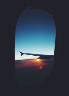 an airplane wing with the sun setting in the sky as seen through it's window