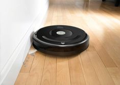 a roomba is laying on the floor next to a white wall and wooden floors