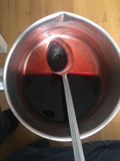 a person is holding a spoon in a pan with red liquid on the bottom and inside