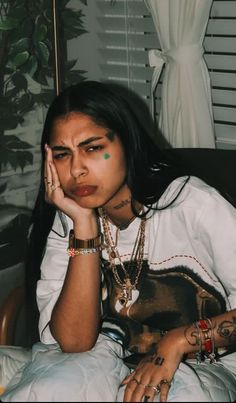 a woman sitting on top of a bed holding her hand to her face and looking at the camera