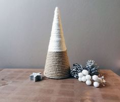 a small knitted christmas tree on a wooden table next to pine cones and balls