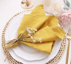 a place setting with yellow napkins and flowers on the plate, along with gold cutlery