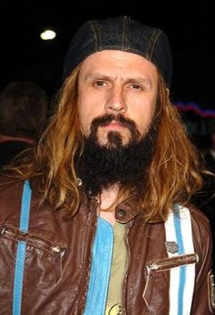 a man with long hair and a beard wearing a leather jacket is looking at the camera