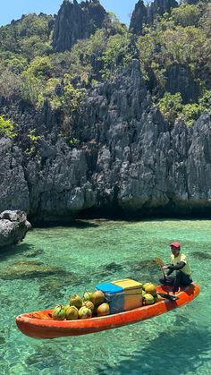 a man in a kayak filled with fruit floating on the water next to rocks