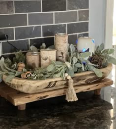 a tray with candles and greenery on top of a counter next to a brick wall