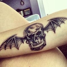 a skull and bat tattoo on the back of a woman's left arm is shown