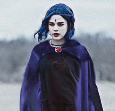 a woman with blue hair wearing a purple cape and black dress standing in the snow