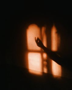 the shadow of a hand on a wall in front of a window with light coming through it