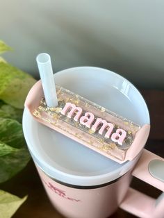 a cup with a straw in it and the word mama written on its lid is sitting next to a plant