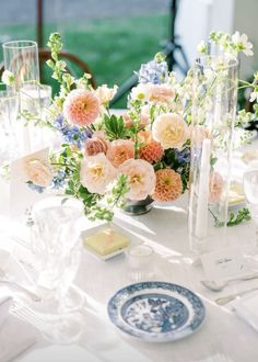 an arrangement of flowers and candles on a white table cloth at a formal dinner party