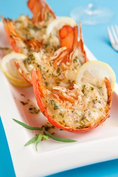 two lobsters on a white plate with lemon wedges and garnishes