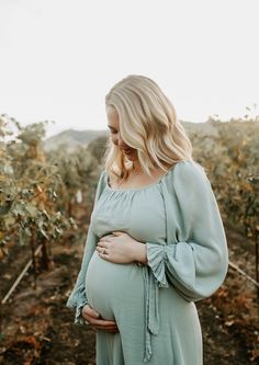 a pregnant woman wearing a blue dress in the vineyard