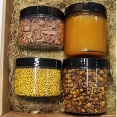 three jars filled with different types of food in a wooden box on top of hay