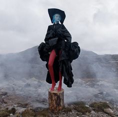 a woman in black dress and red tights standing on top of a tree stump