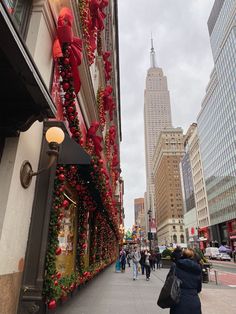 people are walking down the sidewalk in front of a building decorated with christmas decorations and lights