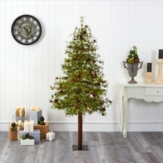 a small christmas tree in the corner of a room with presents and a clock on the wall