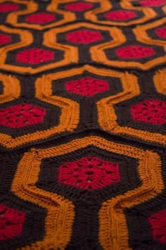 an orange and black crocheted blanket with red flowers on it's edges