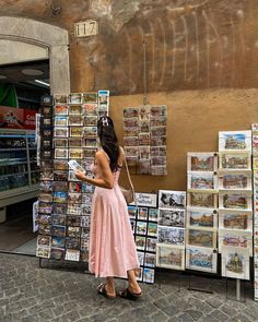 a woman in a pink dress is looking at newspapers on display outside a storefront