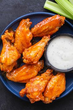 chicken wings with ranch dressing on a blue plate next to celery and celery sticks