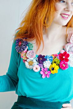 a woman with red hair wearing a blue top and colorful flowers on her neckline