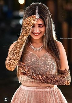 a woman in a dress holding her hands up to her face with henna on