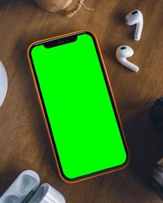 an iphone with a green screen sitting on a table next to ear buds and headphones