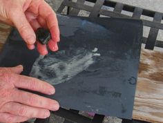 an older person holding a rock in their hand on top of a piece of wood