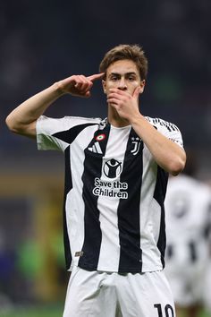 a young man in black and white uniform holding his hand up to his face while standing on a soccer field