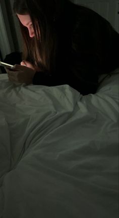 a woman laying in bed looking at her cell phone