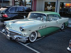 an old green and white car parked in a parking lot next to some other cars