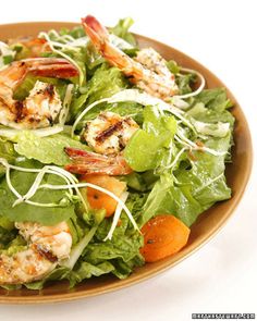 a salad with shrimp, carrots and lettuce in a brown bowl on a white surface