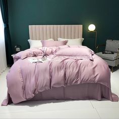 a bed with pink sheets and pillows in a room next to a lamp on the floor