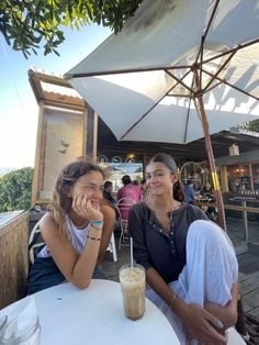 two women sitting at an outdoor table with drinks