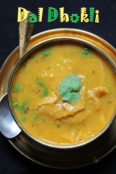 a metal bowl filled with yellow soup and garnished with cilantro leaves