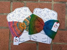 three knitted hats sitting on top of each other next to a brick wall,