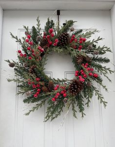 a wreath hanging on the side of a door with pine cones, berries and evergreen