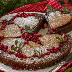 chocolate cake with cranberries and powdered sugar on a platter surrounded by greenery