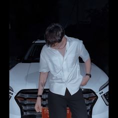 a man in white shirt and black pants standing next to a white car at night