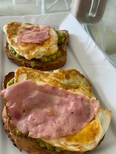 two sandwiches with ham and cheese on them sitting on a white plate, ready to be eaten