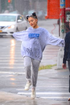 a woman walking down the street in the rain with an oversized sweatshirt over her shoulders