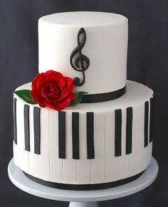 a white cake with piano keys and a red rose