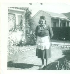 an old black and white photo of a woman standing in front of a house,