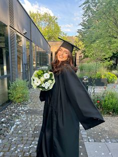 a woman wearing a graduation gown and holding a bouquet of flowers in front of a building